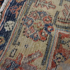 Detailed view of a beige, navy, and red flatwoven rug resting on distressed wood flooring.
