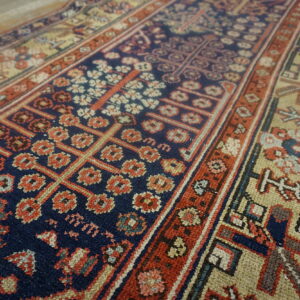 Navy, red, and tan rug showing geometric floral patterns and thick contrasting borders on a floor.