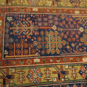 Geometric tribal rug detail showing a navy blue center, rust red border, and khaki yellow motifs.