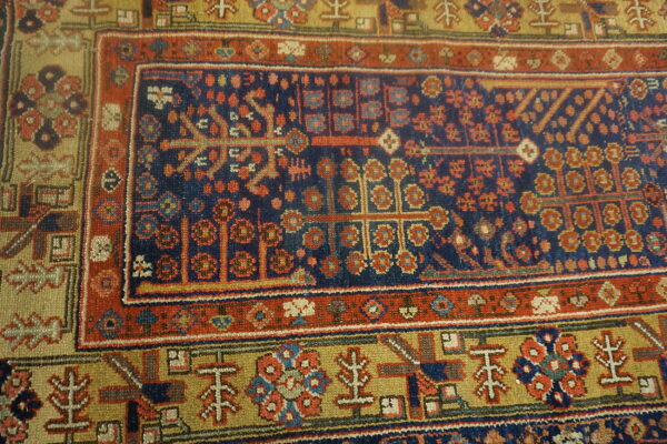 Geometric tribal rug detail showing a navy blue center, rust red border, and khaki yellow motifs.