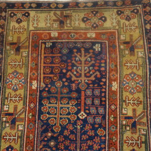 Navy and rust red low-pile rug with dense geometric patterns and olive borders rests on wooden flooring.