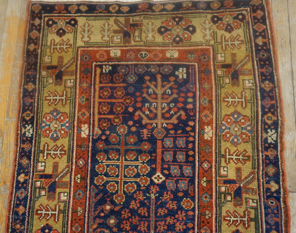 Navy and rust red low-pile rug with dense geometric patterns and olive borders rests on wooden flooring.