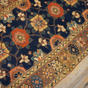 Low-pile rug with navy, rust, and gold traditional patterns rests on distressed wood flooring.