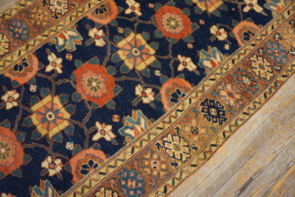 Low-pile rug with navy, rust, and gold traditional patterns rests on distressed wood flooring.