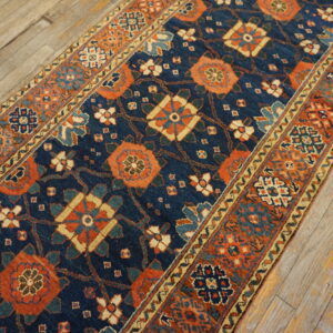 Navy blue runner rug featuring dense orange and teal stylized patterns on rustic plank wood floor.