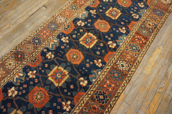 Navy blue runner rug featuring dense orange and teal stylized patterns on rustic plank wood floor.