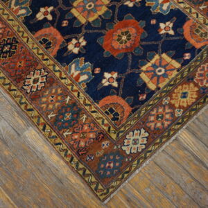A traditional navy rug with rust and gold geometric patterns rests on distressed wooden floor planks.
