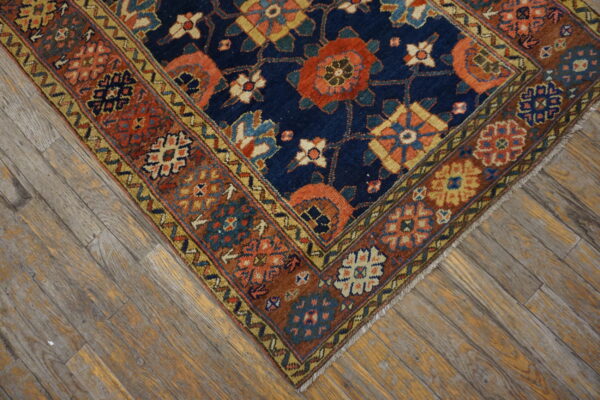 A traditional navy rug with rust and gold geometric patterns rests on distressed wooden floor planks.