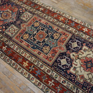 Intricate low-pile runner rug with geometric patterns in navy, rust red, and cream on wood flooring.