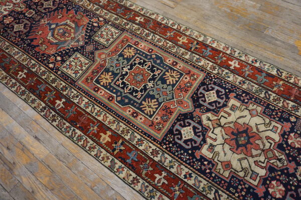 Intricate low-pile runner rug with geometric patterns in navy, rust red, and cream on wood flooring.