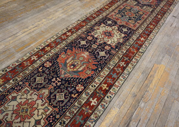 A low-pile runner with navy, red, and cream geometric patterns covers rustic, distressed wood plank flooring.