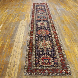 Navy blue and red geometric runner rug lying on a rustic, wide-plank wood floor.