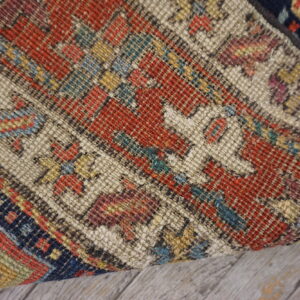 Close-up of a tightly woven rug in geometric red, beige, blue, and yellow on wood flooring.