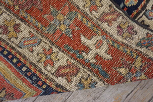 Close-up of a tightly woven rug in geometric red, beige, blue, and yellow on wood flooring.