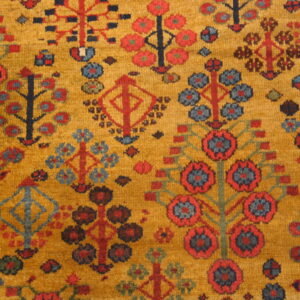 Stylized red, blue, and dark geometric motifs cover a woven mustard gold rug surface.