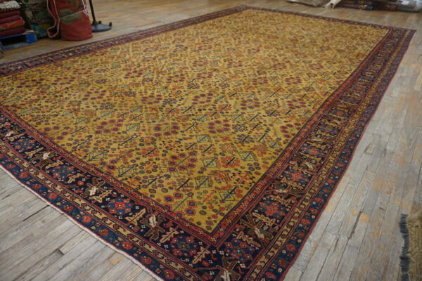 Large traditional rug with a yellow field and navy border rests on greyish-brown plank flooring.