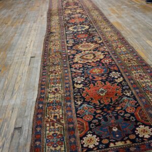 Long runner rug in navy, red, and beige geometric patterns on distressed wood planks.
