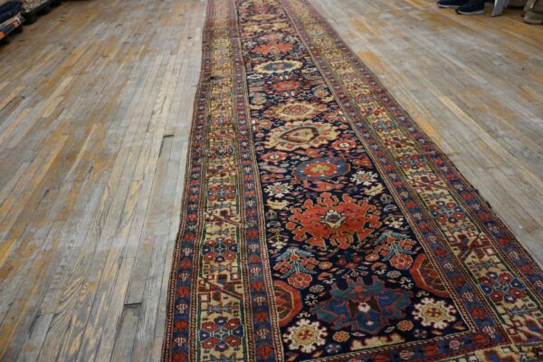 Long runner rug in navy, red, and beige geometric patterns on distressed wood planks.