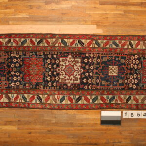 Long runner rug with a navy field, red medallions, and detailed geometric patterns on light wood flooring.