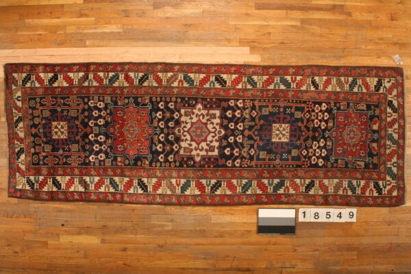 Long runner rug with a navy field, red medallions, and detailed geometric patterns on light wood flooring.