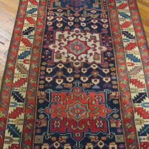A detailed navy and red geometric runner rug rests on worn light brown hardwood floors.
