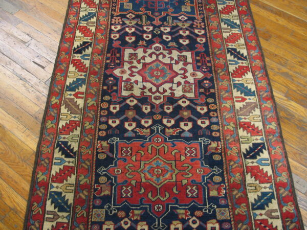 A detailed navy and red geometric runner rug rests on worn light brown hardwood floors.