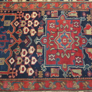 Intricate geometric rug pattern with a navy field, contrasting red motifs, and detailed borders in blue and cream.