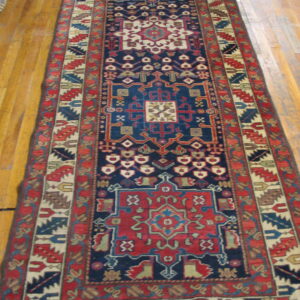 Navy blue and red geometric runner rug with tribal motifs lies on light brown hardwood flooring.