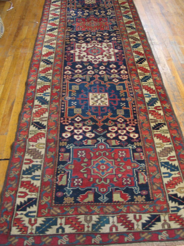 Navy blue and red geometric runner rug with tribal motifs lies on light brown hardwood flooring.