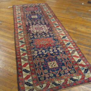 Deep blue and red patterned runner rug with multiple geometric borders rests on shiny wood planks.