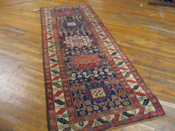 Deep blue and red patterned runner rug with multiple geometric borders rests on shiny wood planks.