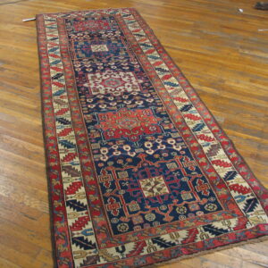 A long, dark blue runner rug with intricate red and cream geometric motifs rests on worn wood planks.