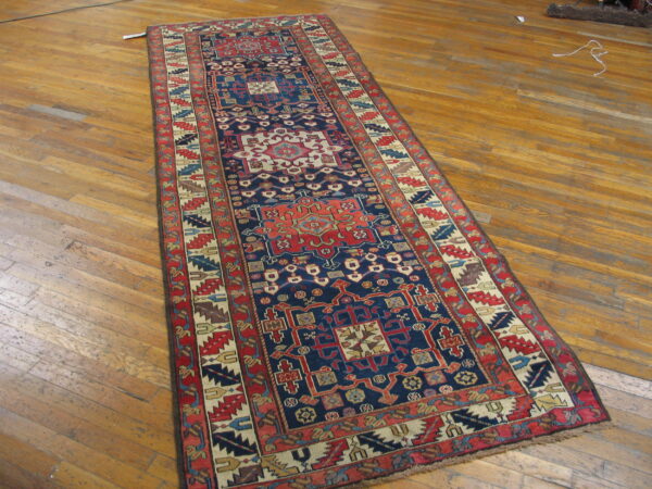 A long, dark blue runner rug with intricate red and cream geometric motifs rests on worn wood planks.