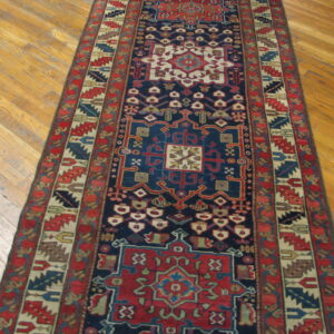 Navy blue runner rug with red, cream, and green geometric motifs rests on light wood floor planks.