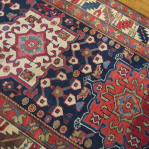 Geometric navy, red, and cream patterned rug runner detailed close-up resting on wood floors.