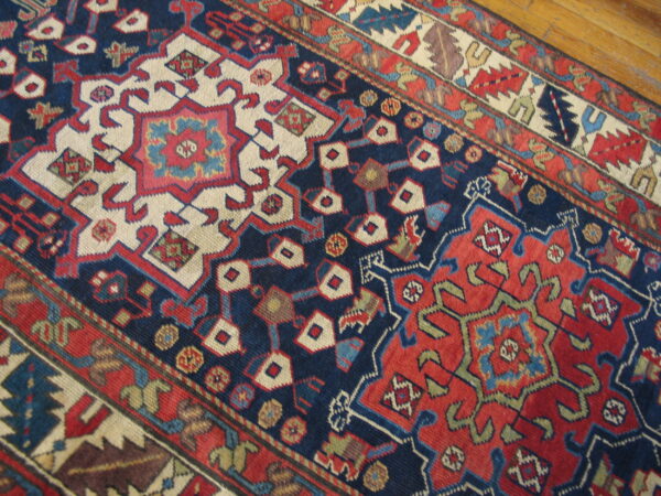 Geometric navy, red, and cream patterned rug runner detailed close-up resting on wood floors.