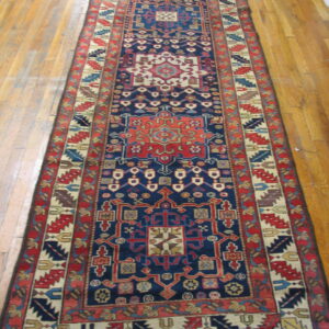 Navy blue and red patterned runner rug with geometric medallions lying on light wood planks.