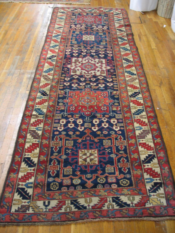 Navy blue and red patterned runner rug with geometric medallions lying on light wood planks.