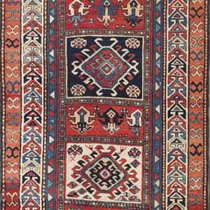 Narrow runner rug featuring repeating geometric medallions in red, navy blue, and off-white fields.