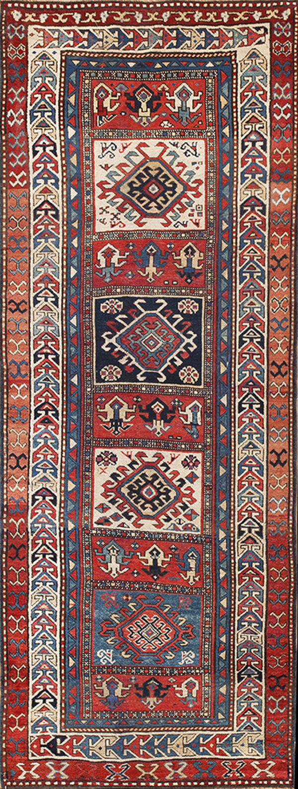 Narrow runner rug featuring repeating geometric medallions in red, navy blue, and off-white fields.