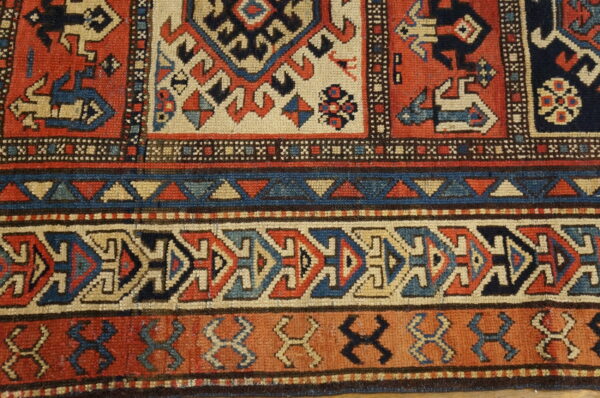 Geometric rug detail featuring dense borders and motifs in terracotta, navy, tan, and light blue resting on a wood floor.
