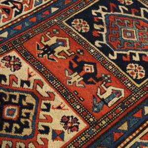 Detailed view of a dense, low-pile rug patterned with alternating navy, rust red, and cream medallions.