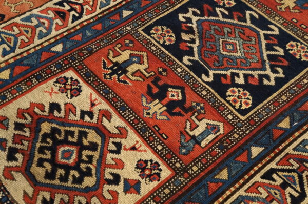 Detailed view of a dense, low-pile rug patterned with alternating navy, rust red, and cream medallions.