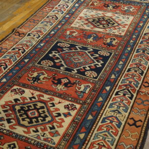 Geometric runner in navy, rust, and cream with repeating square medallions rests on aged hardwood flooring.