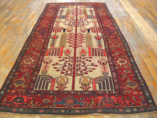 Traditional red and beige runner rug featuring stylized tree motifs and geometric borders on light hardwood flooring.