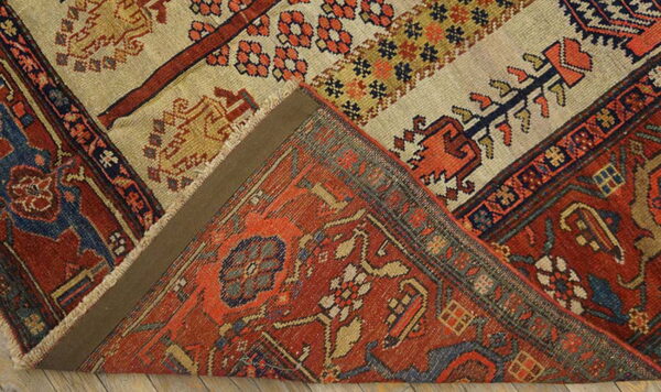 A rust-colored rug with complex patterns is folded to show the beige and striped flat-woven reverse.