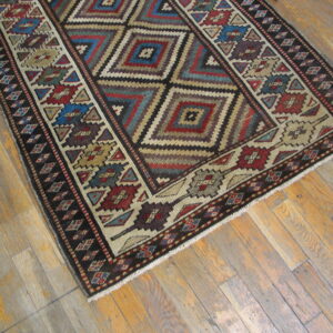 A multicolored tribal geometric rug featuring nested diamond motifs rests on distressed wood plank flooring.