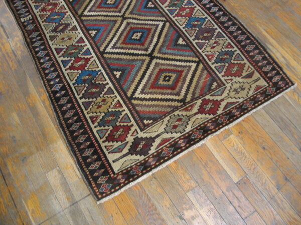 A multicolored tribal geometric rug featuring nested diamond motifs rests on distressed wood plank flooring.
