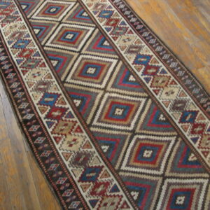 Geometric runner rug with nested diamonds in red, blue, and brown on a wood plank floor.