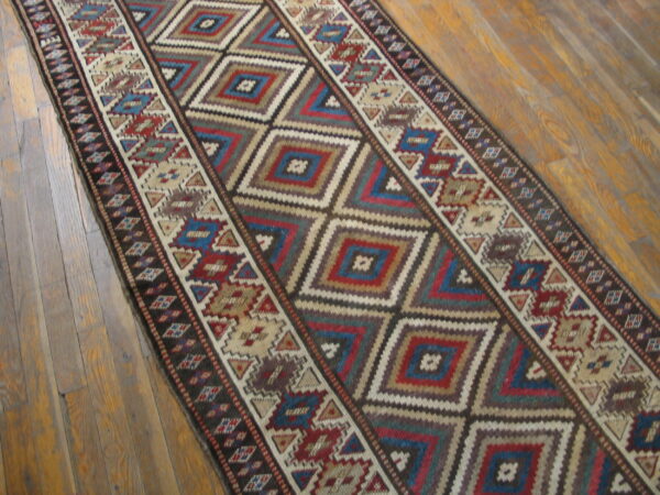 Geometric runner rug with nested diamonds in red, blue, and brown on a wood plank floor.